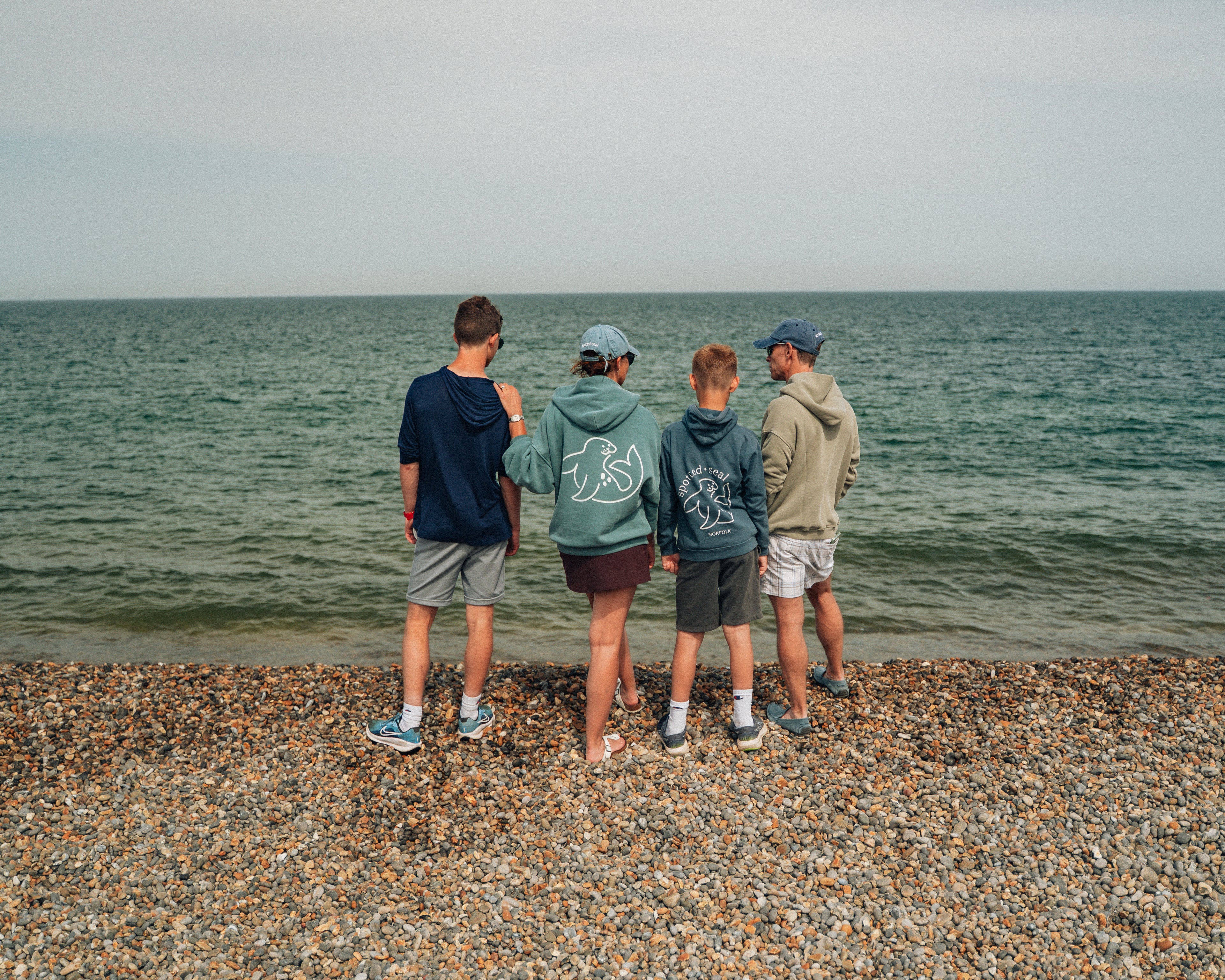 Family standing on a pebbly beach looking out at the ocean in spotted-seal clothing.