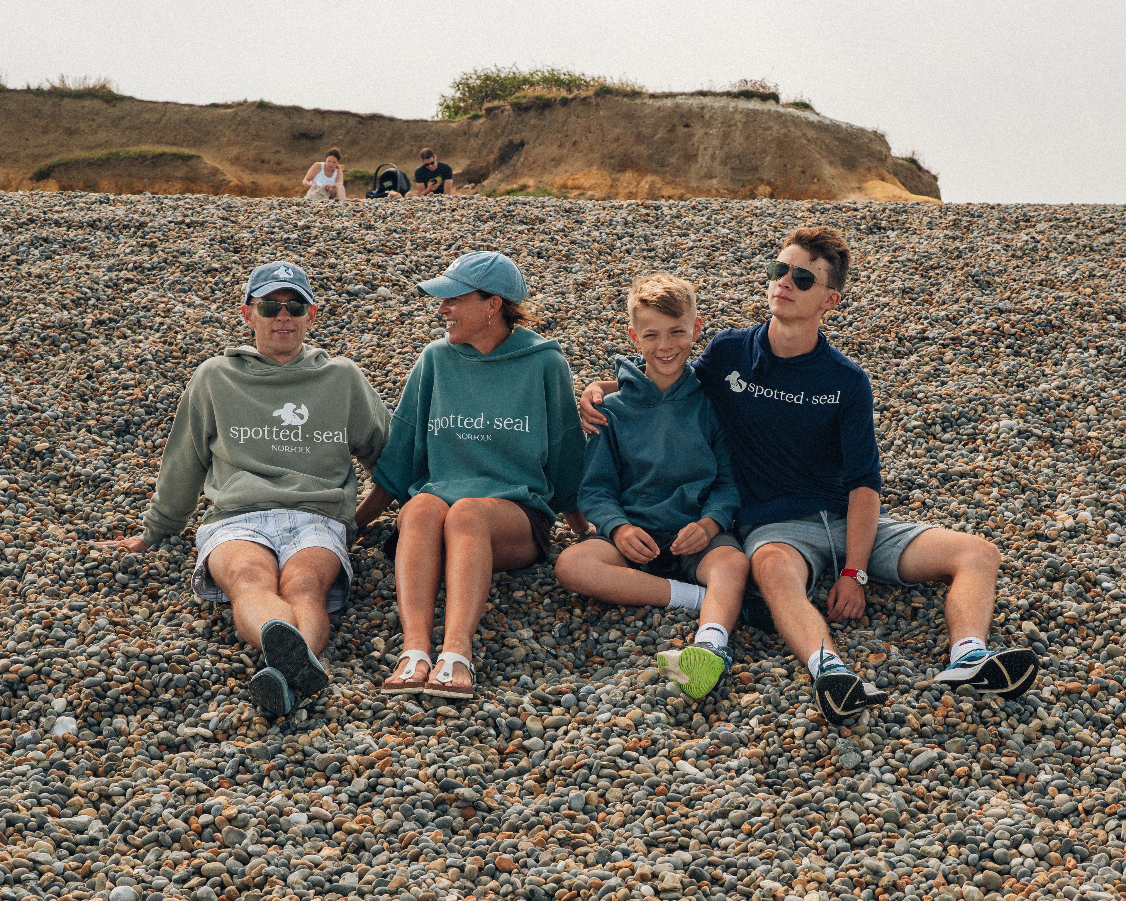 family sitting on shingle beach in spotted-seal hoodies and caps