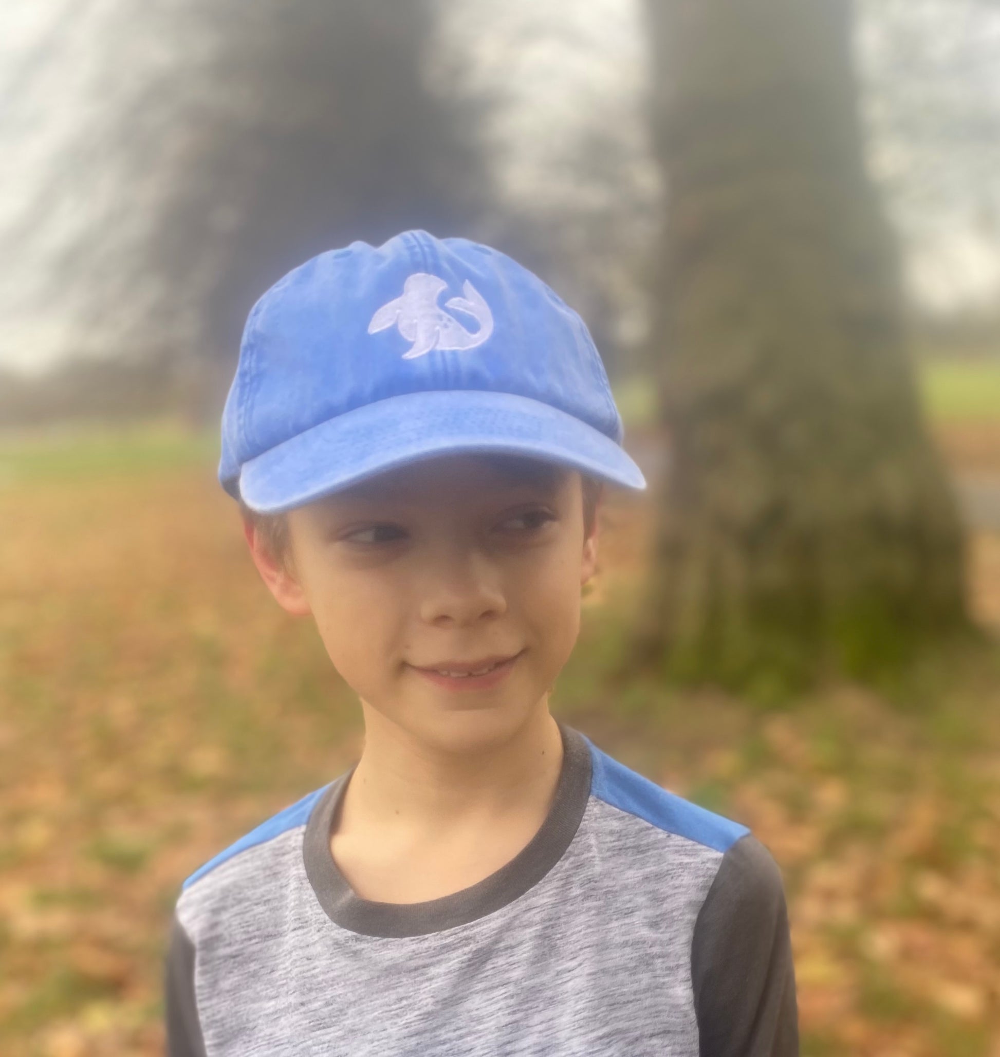 model in spotted-seal unisex cap in cornflower blue Stiffkey skies with seal embroidered on front 