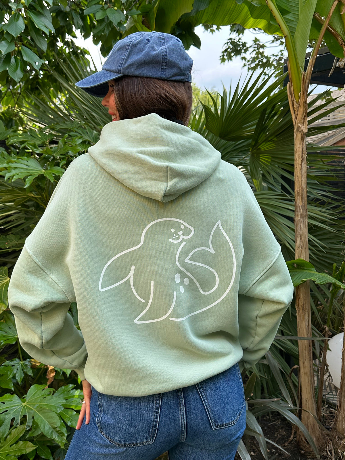 model showing back of women's spotted-seal slouch hoodie in sea foam green with seal on back